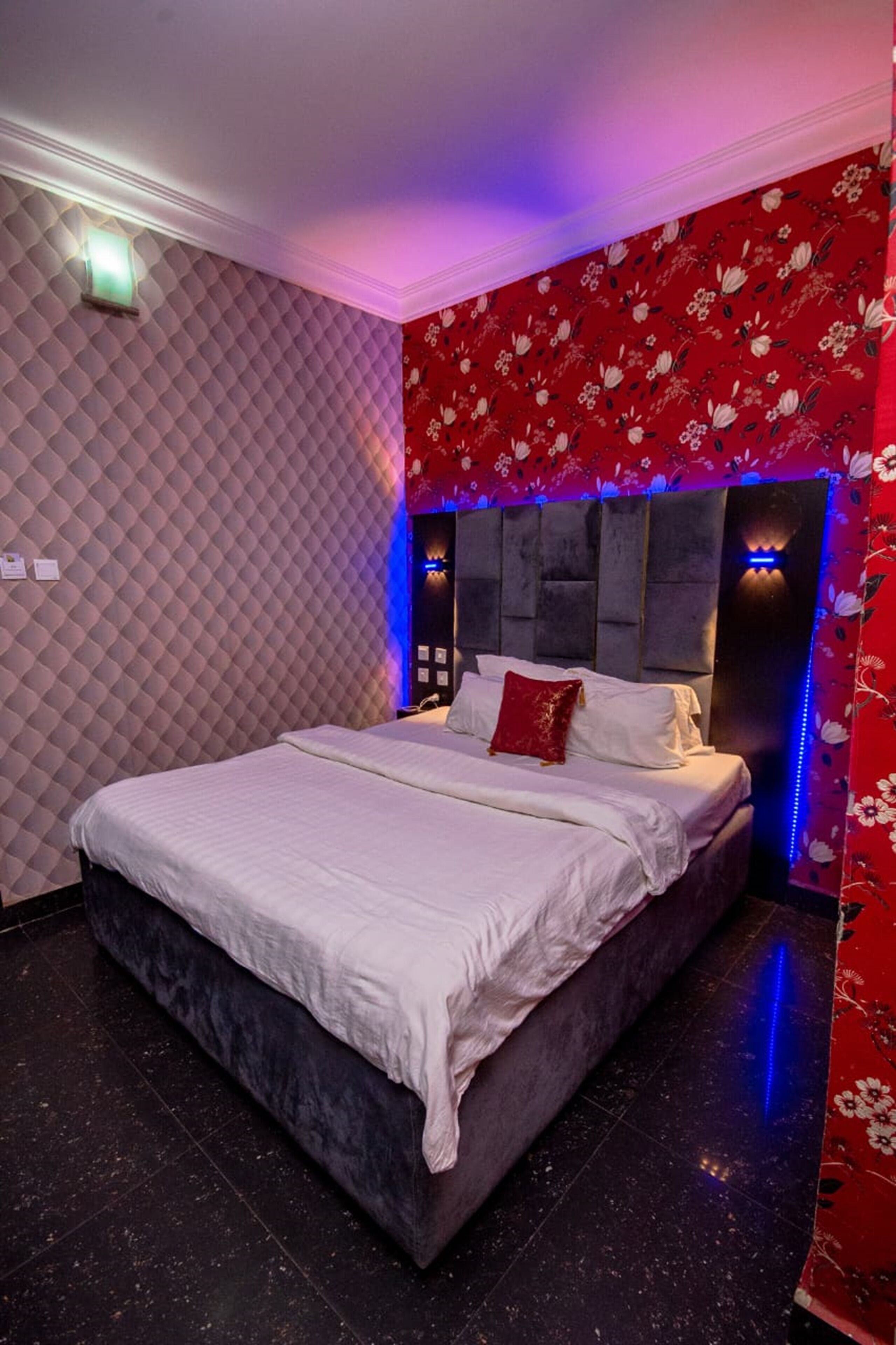 A bedroom with a large bed, a headboard with built-in lighting, and a patterned wall.