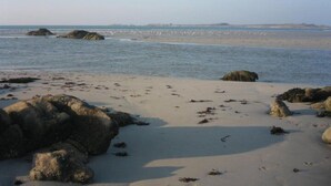 A sandy beach with large rocks and calm water.