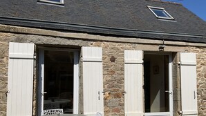 A stone building with two open doors and a table with chairs outside.
