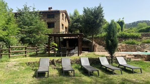 Un bâtiment rustique en pierre, doté d’une pergola en bois et d’un espace extérieur aménagé avec des fauteuils confortables.