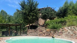 Une piscine en pierre, dotée d’une terrasse en bois et d’un escalier en pierre menant à un bâtiment.
