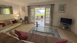 Ein Wohnzimmer mit Sofa, Couchtisch, Fernseher und Blick ins Freie durch eine Glastür.