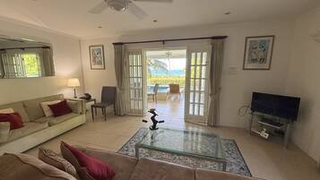 Ein Wohnzimmer mit Sofa, Couchtisch, Fernseher und Blick ins Freie durch eine Glastür.