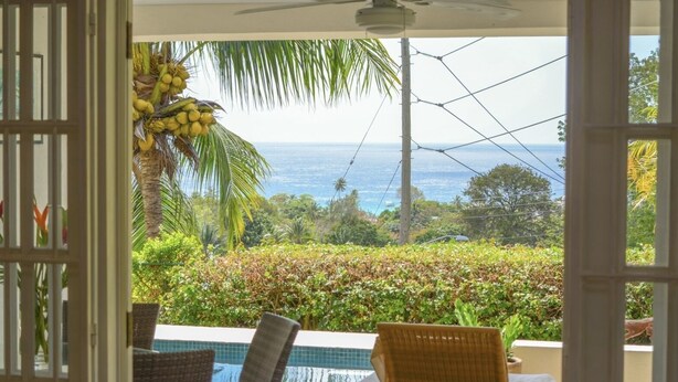 Blick von einem Zimmer mit Pool, inklusive Stuhl, Tisch und Blick auf das Meer und Grünflächen.