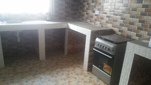 A kitchen with a gas stove, oven, and tiled backsplash. - Permiss Ka Apartments (Accra)