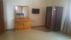 A room with a wooden dresser, a flat-screen TV mounted on the wall, and a wardrobe. - Permiss Ka Apartments (Accra)