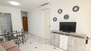 Eine moderne Küche mit integriertem Fernseher, eine Essecke mit Glastisch und Stühlen sowie ein Wohnbereich mit einer Couch.