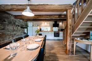 A dining area with a wooden table set for a meal, a stone wall, and a staircase leading to an upper level.