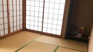 Une pièce avec un sol recouvert de tatamis, une porte coulissante et une petite étagère sur laquelle sont posés quelques objets.