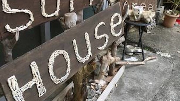 Un espace extérieur rustique agrémenté d’une enseigne en bois sur laquelle on peut lire « SUGAR HOUSE » et d’une autre enseigne indiquant un « espace fumeurs ».