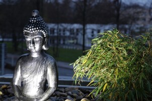 Una estatua de una figura sentada, posiblemente Budha, en un jardín con un montón de follaje verde cerca.