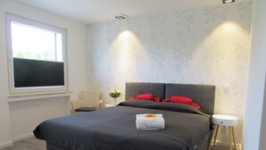 A modern bedroom with a large bed, a chair, a bedside table, and a window. - Minsu Hotel (Muelheim an der Ruhr)