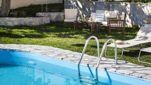 En swimmingpool med stenbord, en liggestol, et træbord og en stenvæg med bænk.
