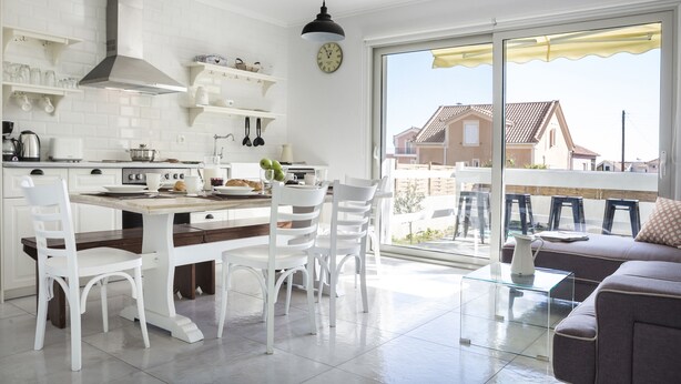 Et moderne køkken med hvide skabe, et spiseområde med hvide stole og en balkon med sofa og stole.