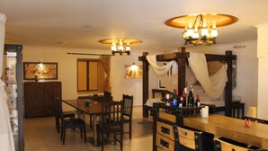 A dining area with a wooden table and chairs, a chandelier, and a painting on the wall. - Dodo's Santorini (Santorini)