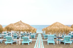 A beach with rows of blue lounge chairs and thatched umbrellas, leading to the ocean. - Dodo's Santorini (Santorini)