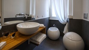 Une salle de bain moderne avec deux grands lavabos blancs, des toilettes rondes et un meuble-lavabo en bois surmonté de deux verres.
