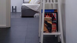 Une chambre d’hôtel moderne, avec un lit, une petite table blanche sur laquelle sont posés des magazines, et une porte qui donne sur une autre pièce.