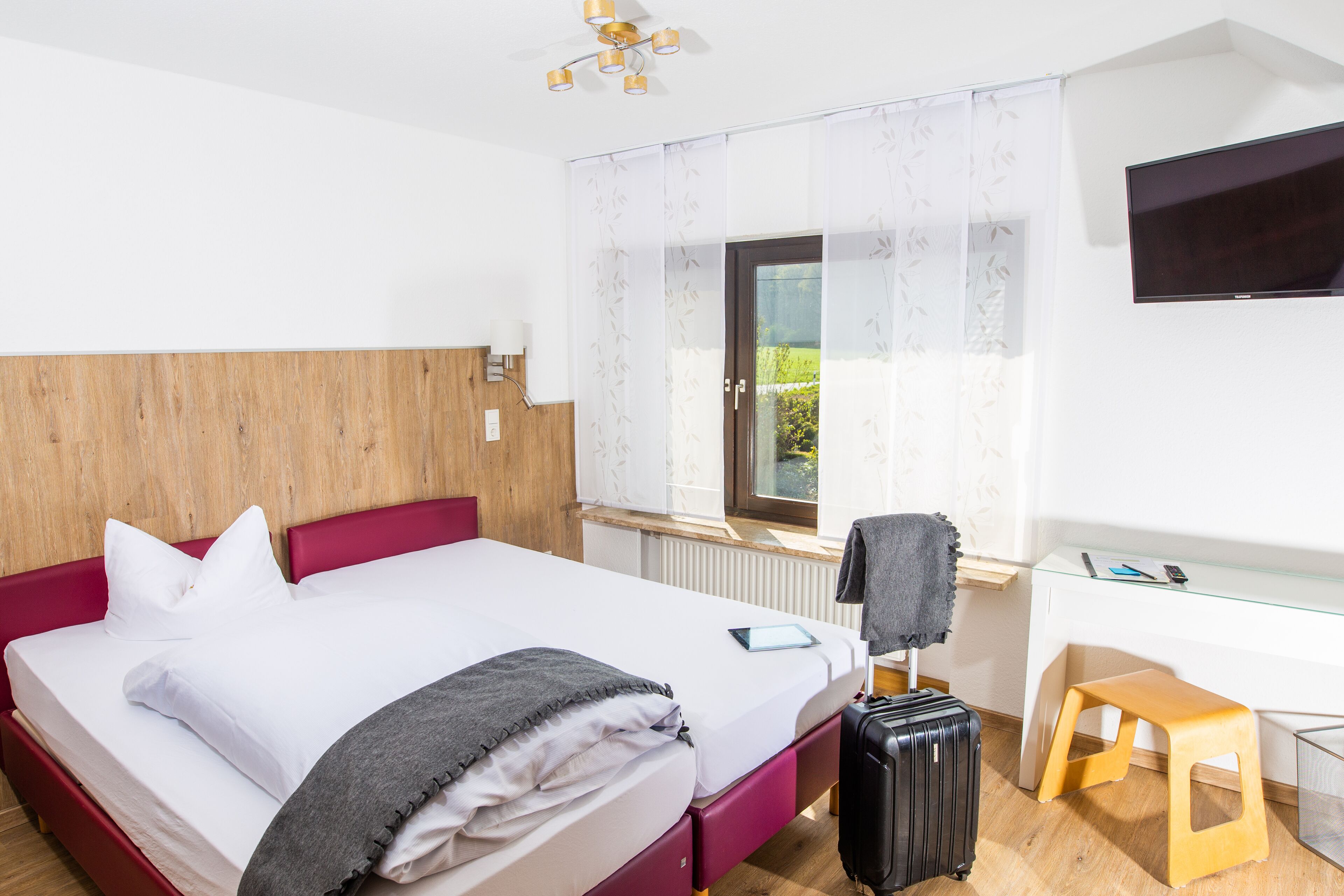 A hotel room with a bed, a desk, a chair, a TV, and a suitcase.
