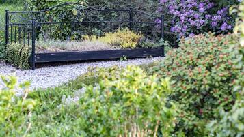 Ein Garten mit einer schwarzen Metallbank, umgeben von verschiedenen Pflanzen und Blumen.