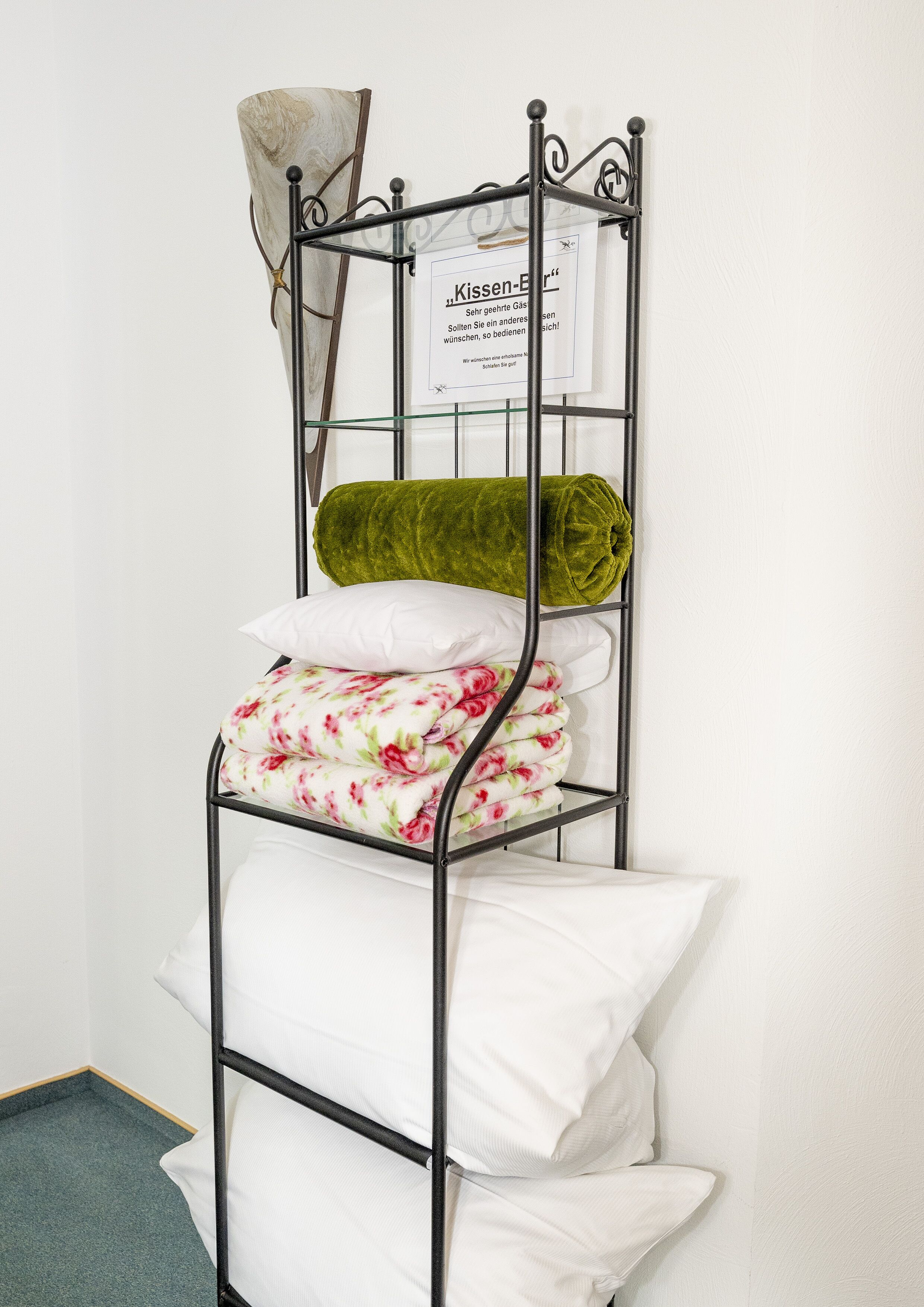 Ein Metallstockbett mit weißer und floraler Bettwäsche, einer grünen Decke und einem Schild an der Wand.