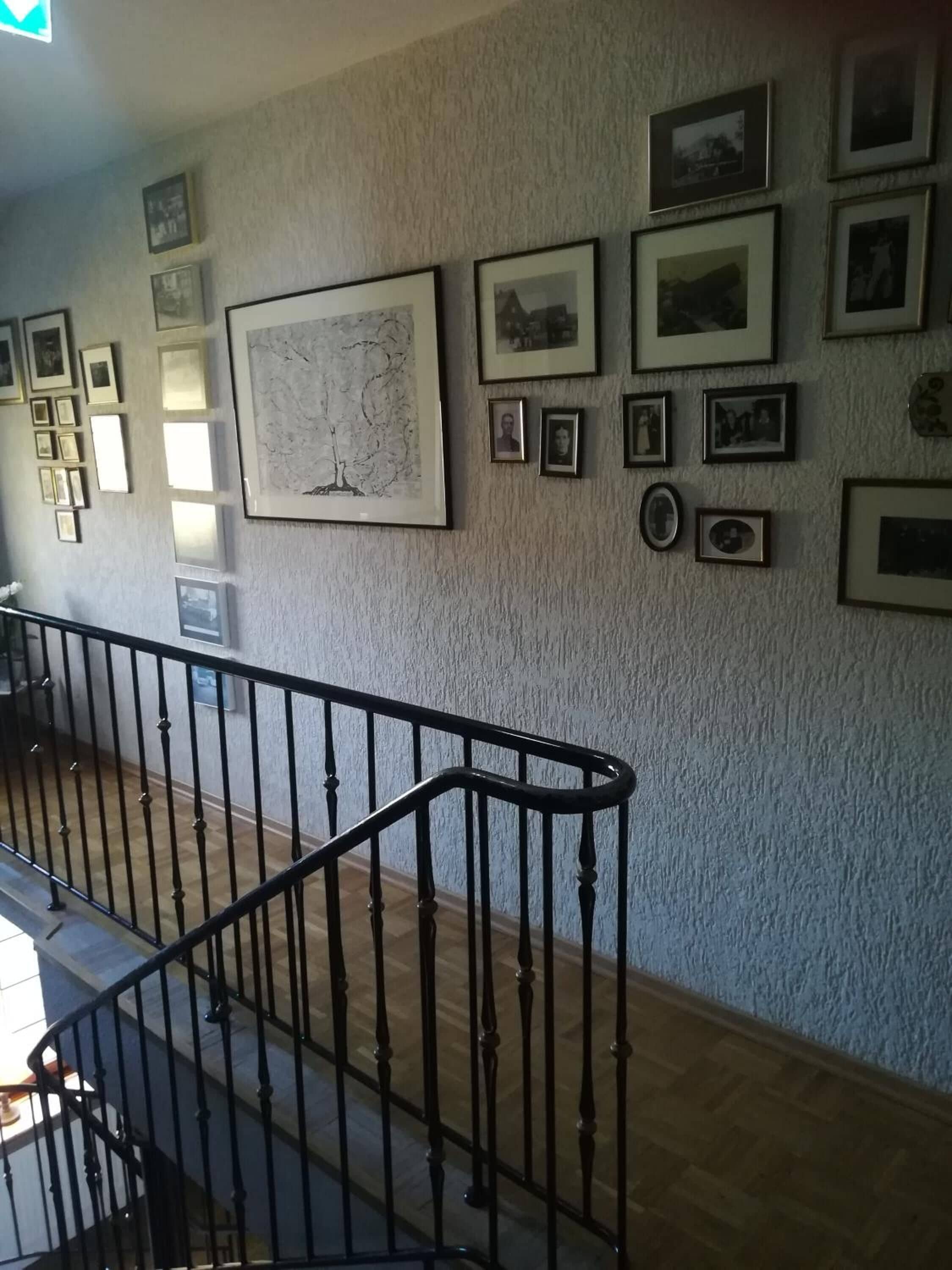 A staircase with a black railing leading to an upper floor. The wall is adorned with numerous framed photographs and a large framed artwork.