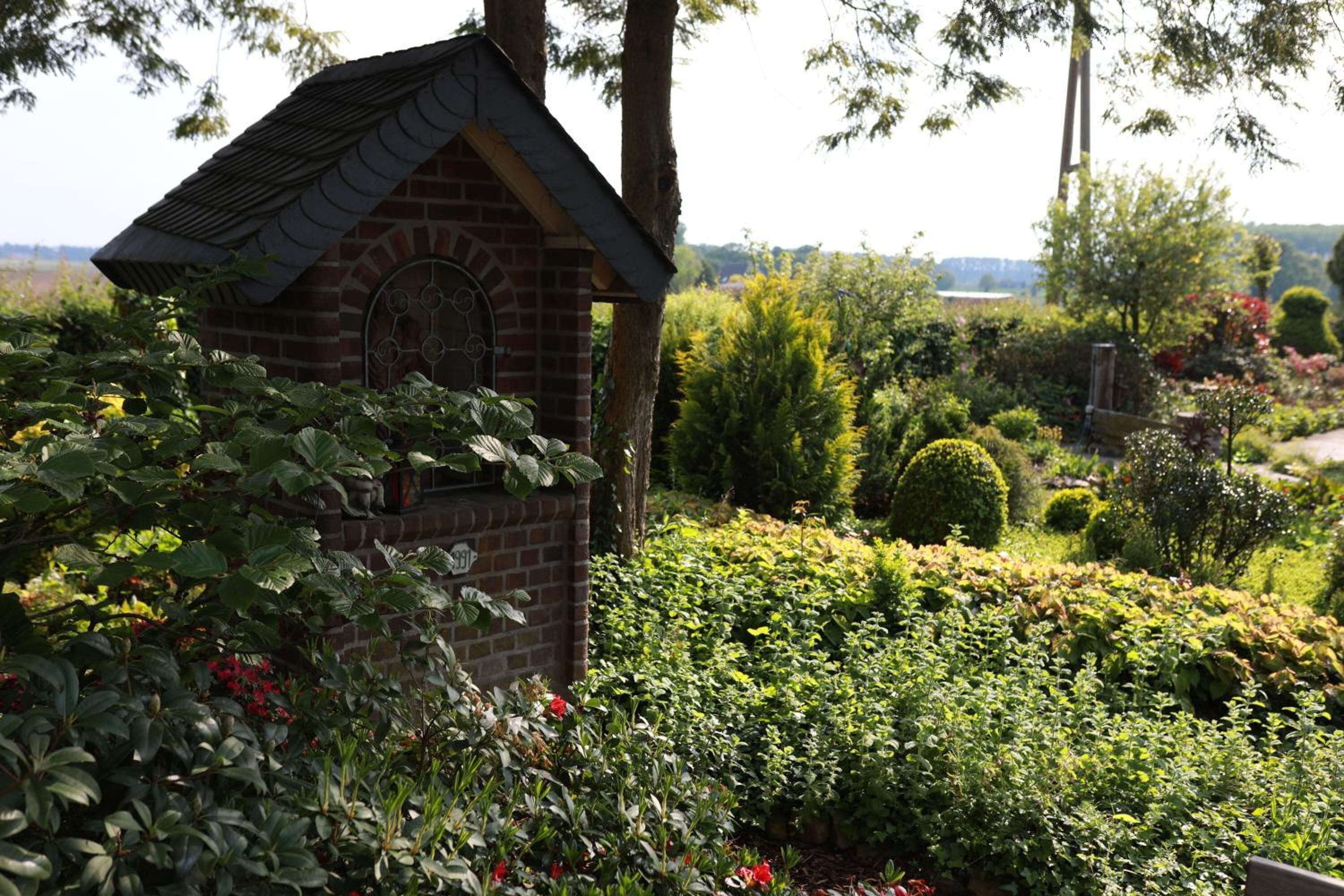 A brick structure with a decorative window, surrounded by lush greenery and various plants.