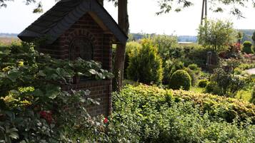 A brick structure with a decorative window, surrounded by lush greenery and various plants.