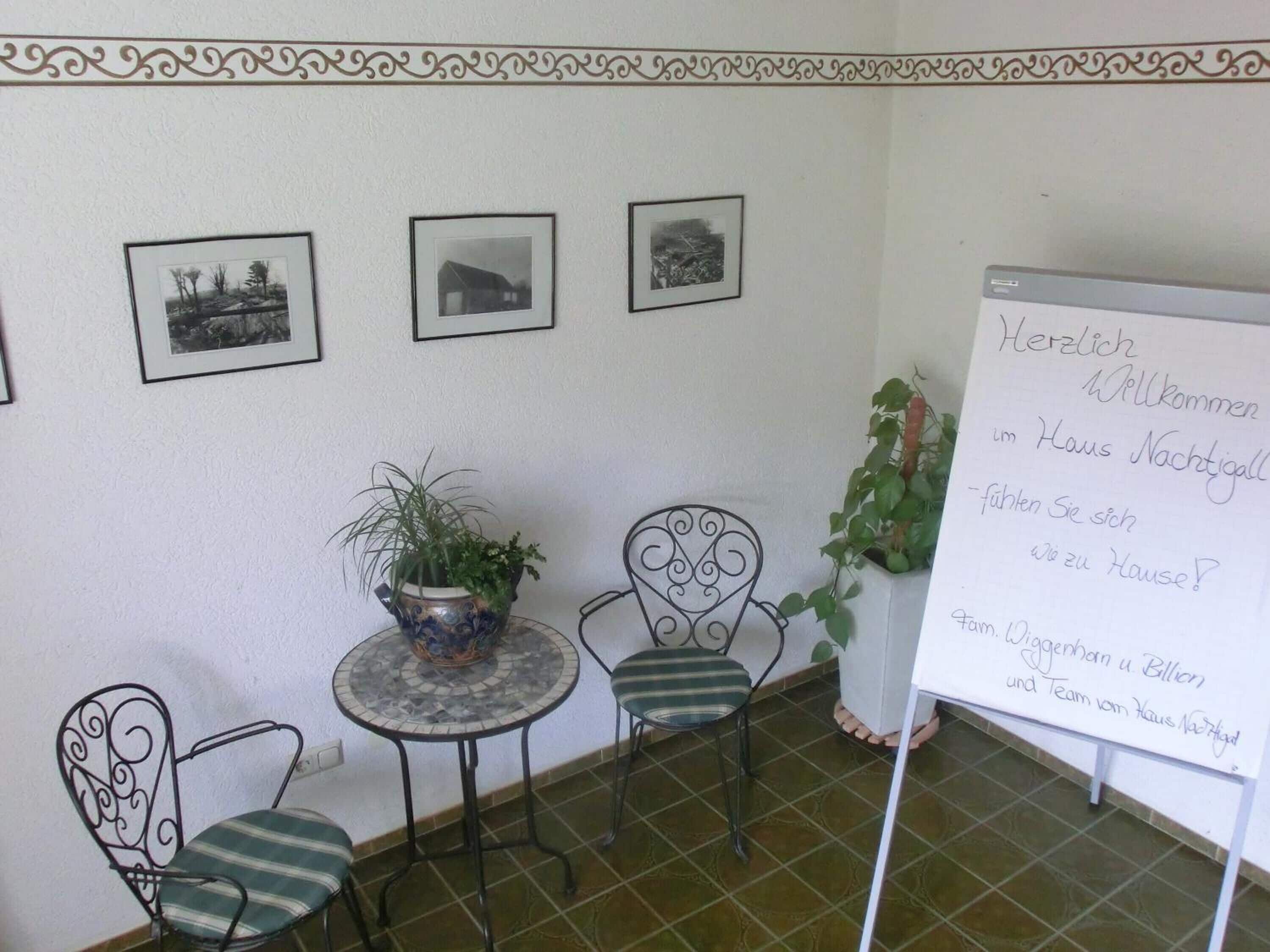Una habitación pequeña con una pizarra, dos sillas, una mesa y tres cuadros en la pared.