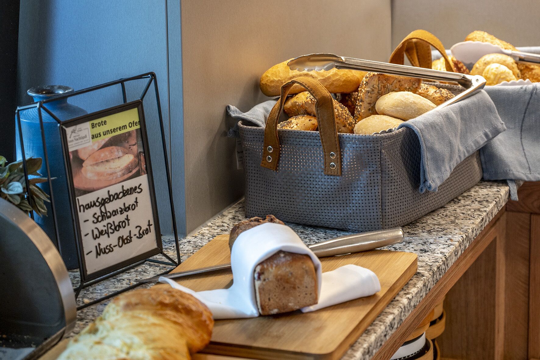 Un bufé de desayuno con panes y bollería diversos, un cartel con opciones de menú y una máquina de café.