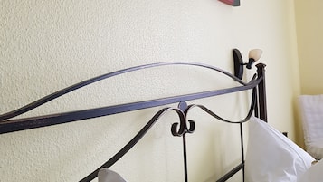 Una cama con ropa de cama blanca y cabecero de metal en una habitación con paredes amarillas y un cuadro de flores.