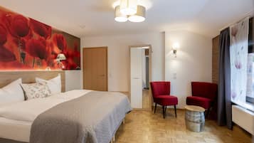 A hotel room with a bed, two red chairs, a small round table, a mirror, and a window with curtains.