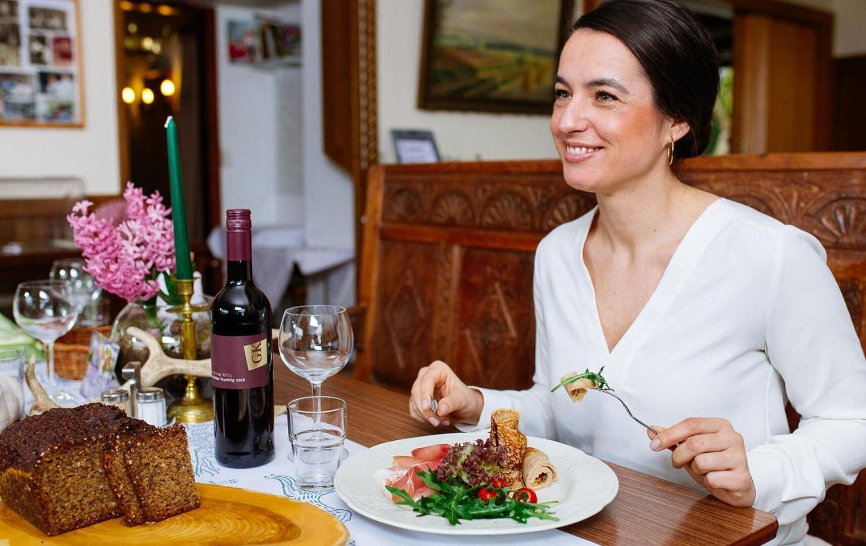Una persona dinant a taula amb una ampolla de vi, una barra de pa i un plat de menjar.