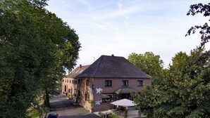 Un bâtiment en briques de deux étages, doté d’un toit en pente, d’un espace extérieur couvert avec des sièges et d’une allée pavée où sont garées des voitures.