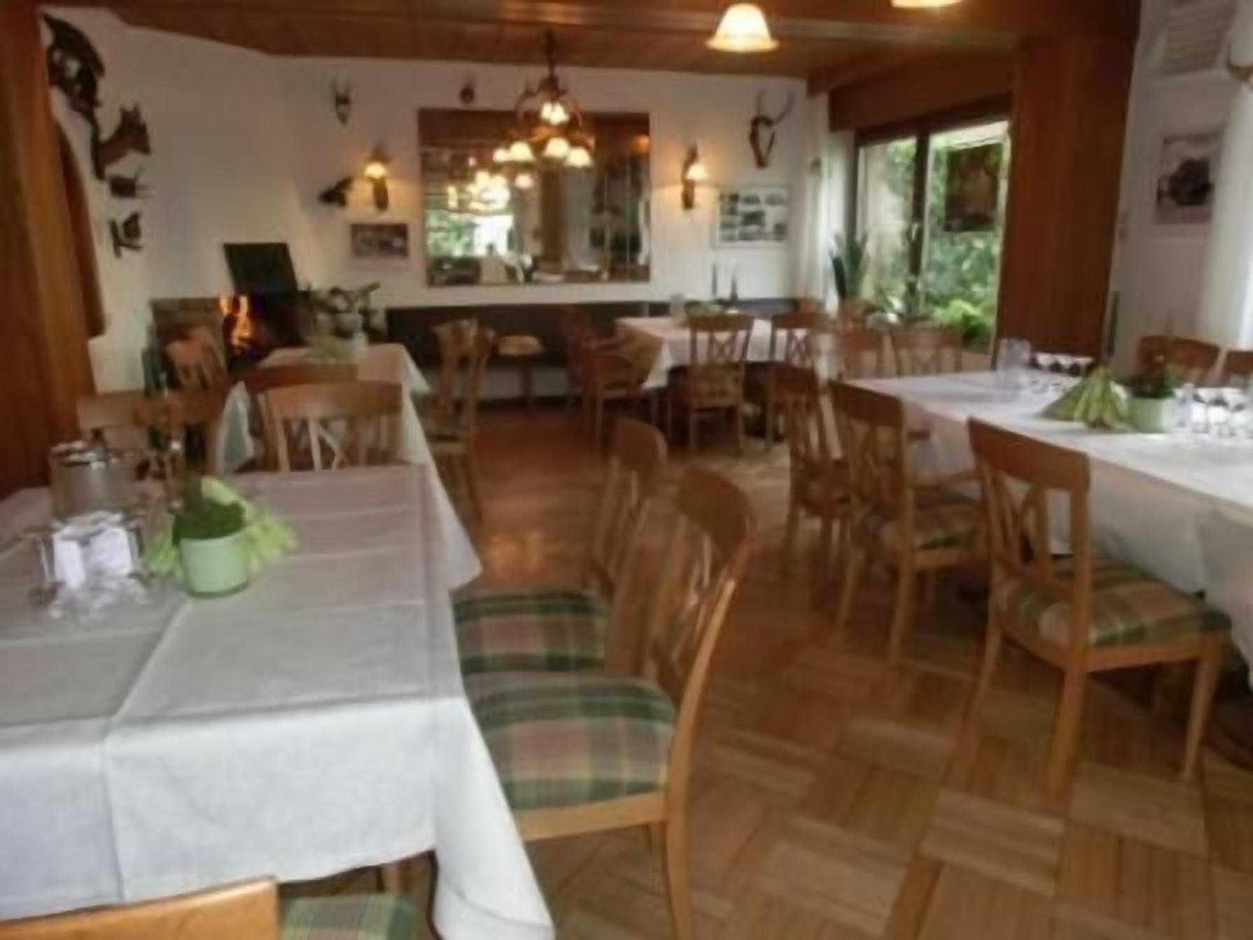 Un comedor con varias mesas y sillas, suelo de madera y vistas al exterior a través de amplios ventanales.