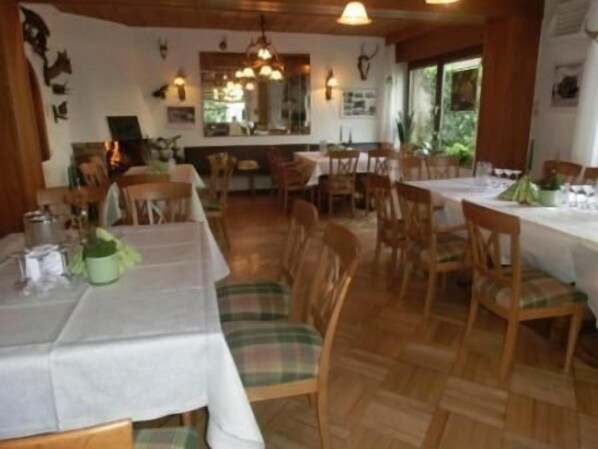 Un espace repas comprenant plusieurs tables et chaises, un plancher en bois et une vue sur l’extérieur grâce à de grandes fenêtres.