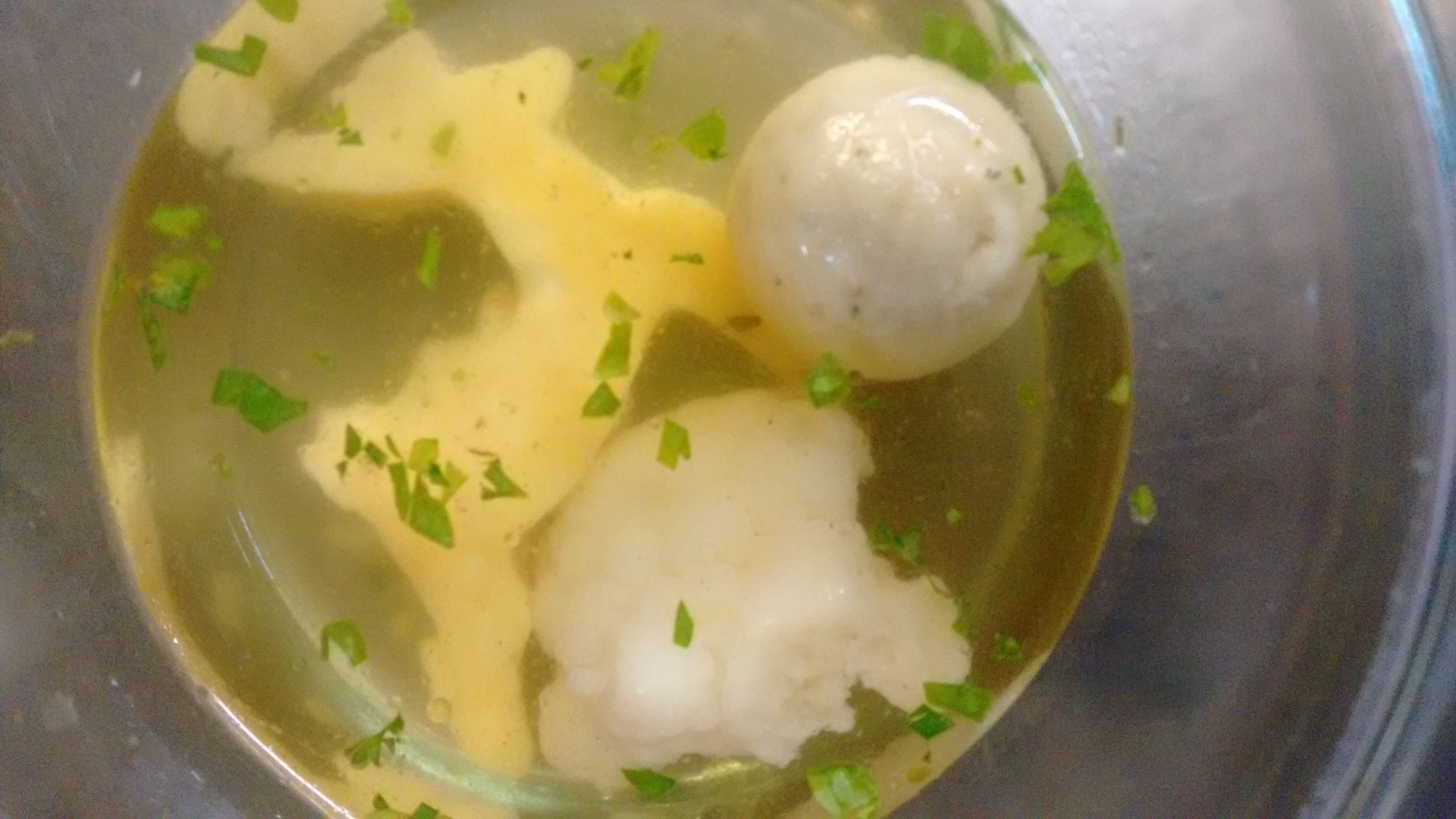 A bowl of soup with dumplings and chopped herbs.