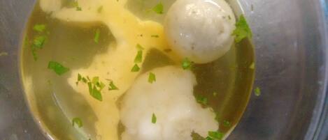 A bowl of soup with dumplings and chopped herbs.