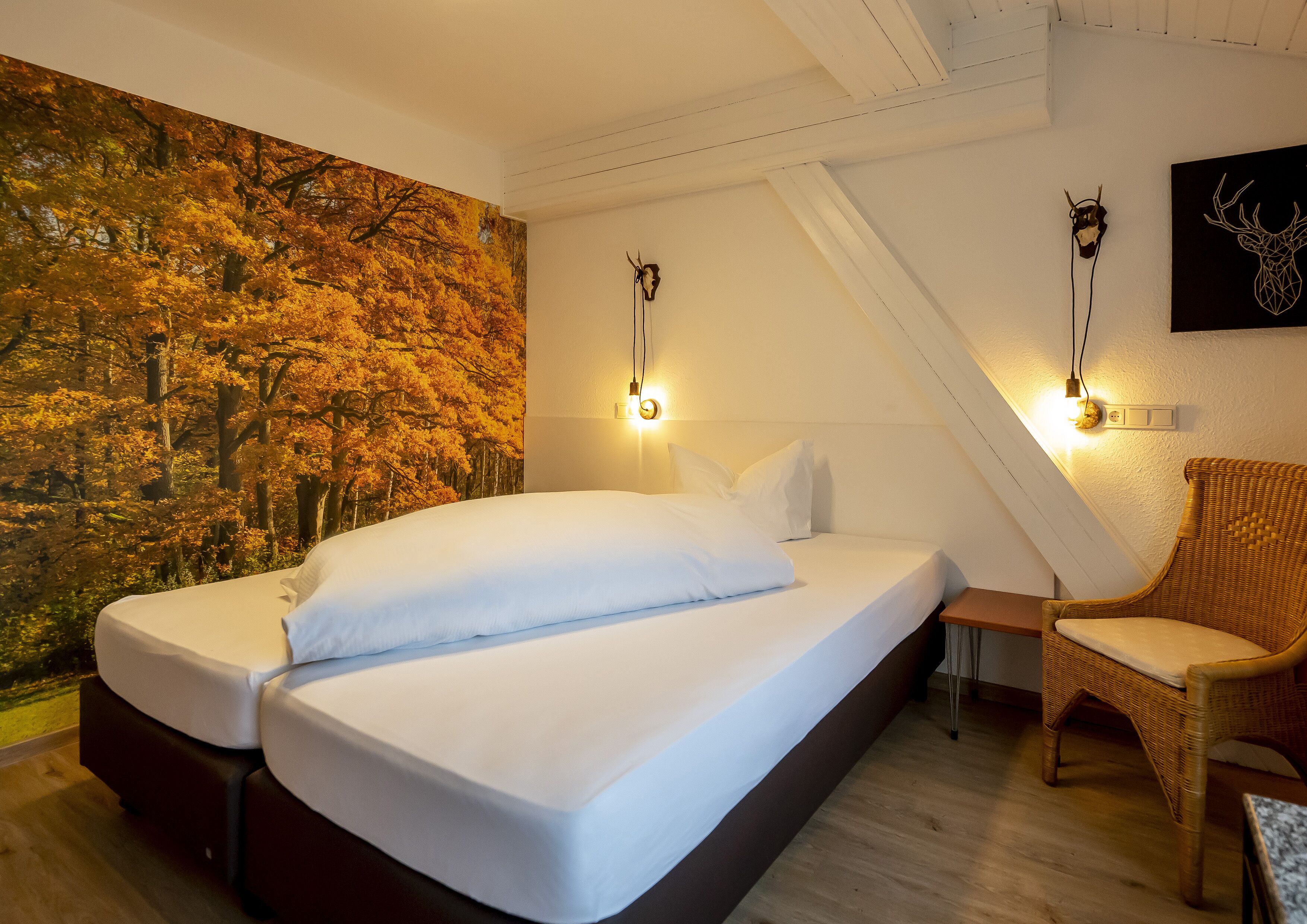 A bedroom with a bed, a chair, a wall-mounted light, and a forest mural.