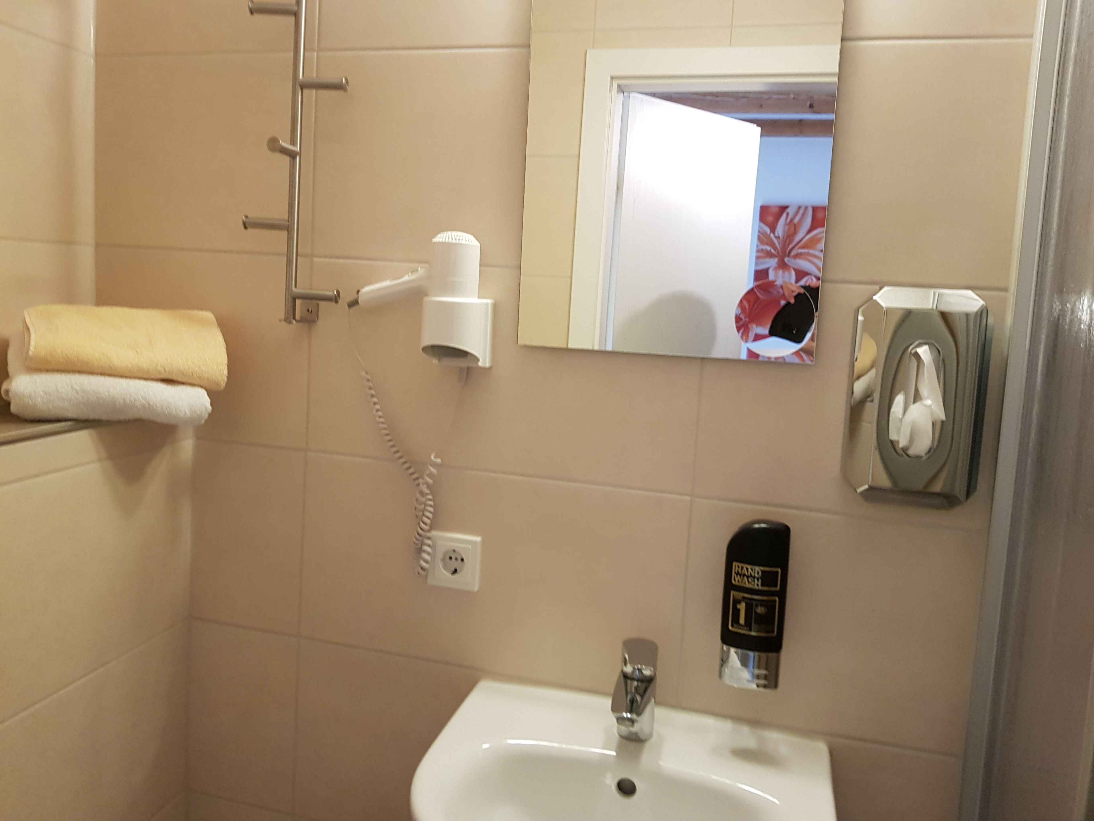 Un baño con lavamanos, secamanos y perchero para toallas.