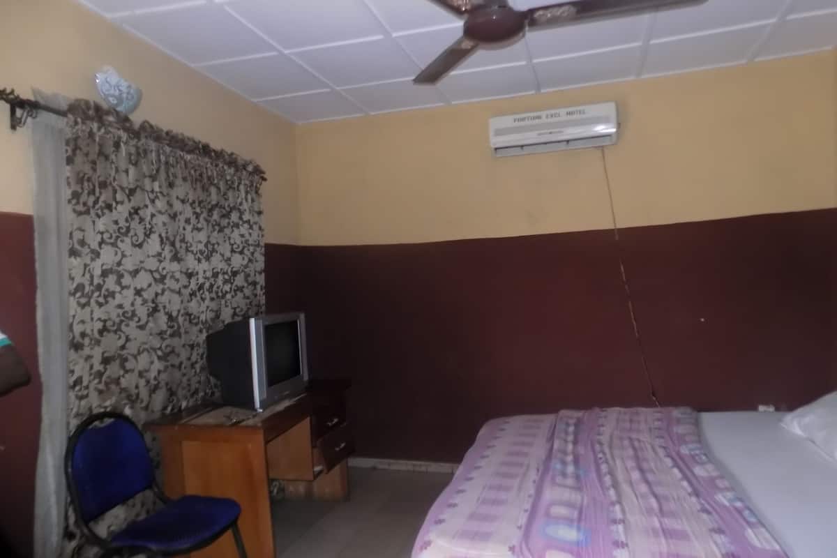 A bedroom with a bed, a desk with a television, a ceiling fan, and an air conditioning unit.