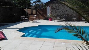 Una piscina con suelo de baldosas, rodeada de mobiliario exterior y un muro de piedra.