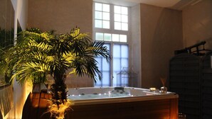 Un área de spa con un jacuzzi, una palmera en maceta y una ventana con vidrio esmerilado.