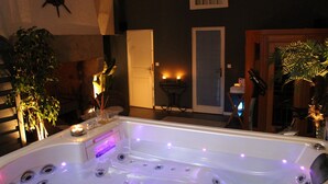 Un área de spa con un jacuzzi, plantas y una puerta que da a otra habitación.