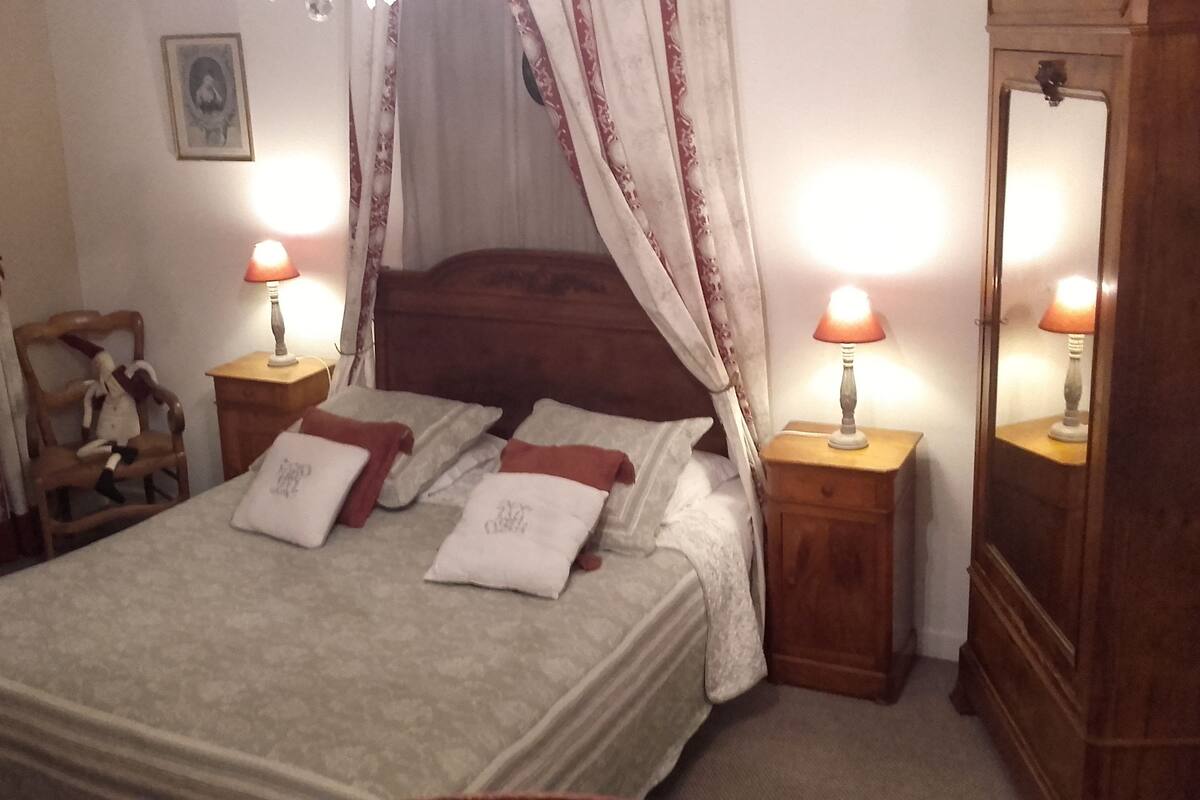 A bedroom with a bed, two nightstands, a wooden chair, and a mirror.