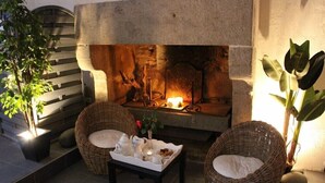 Un rincón exterior acogedor con sillas de mimbre, una pequeña mesa con una bandeja de té y aperitivos, y una chimenea.