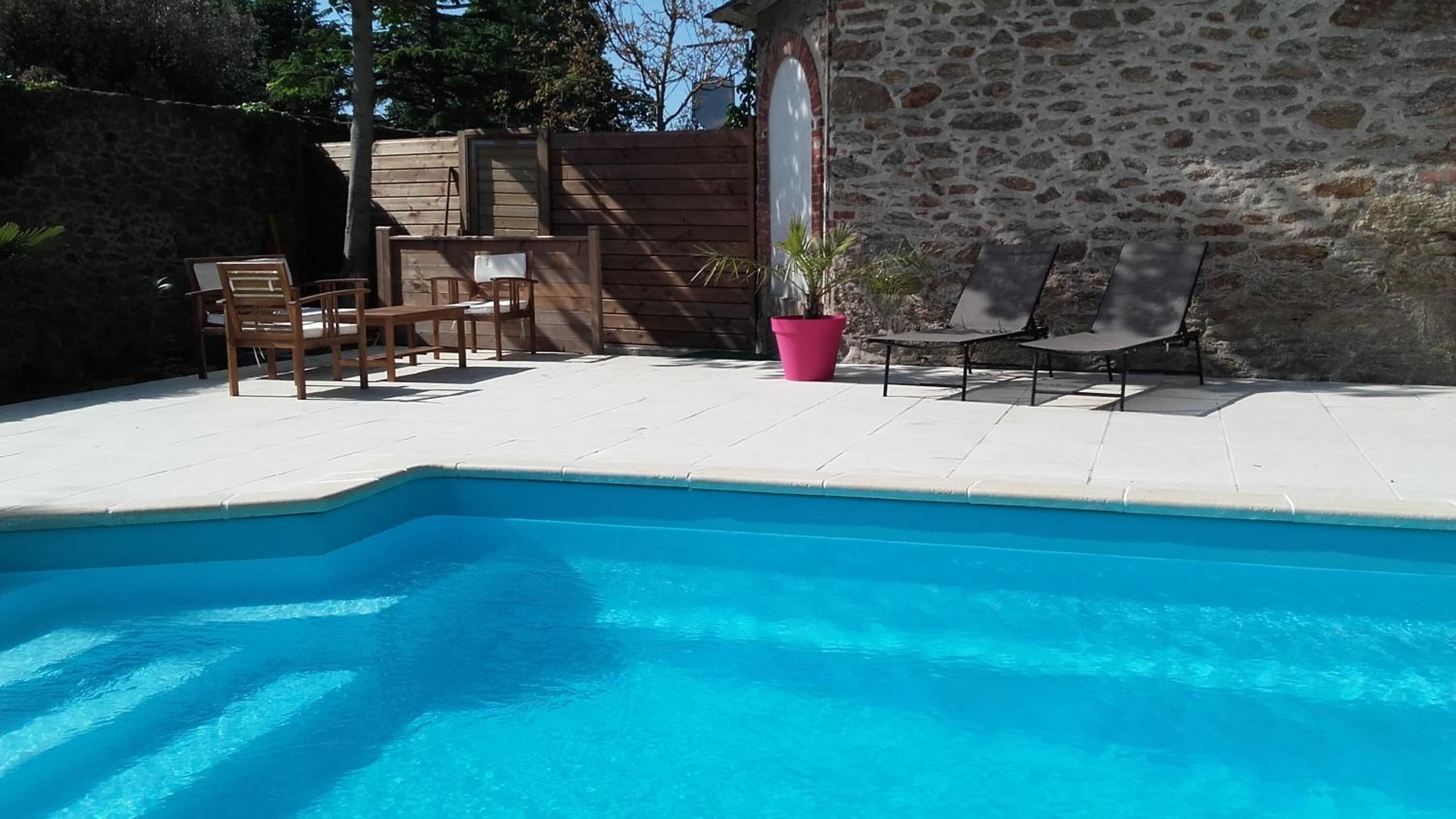 Una piscina con muelle de madera, pared de piedra y mobiliario de exterior.