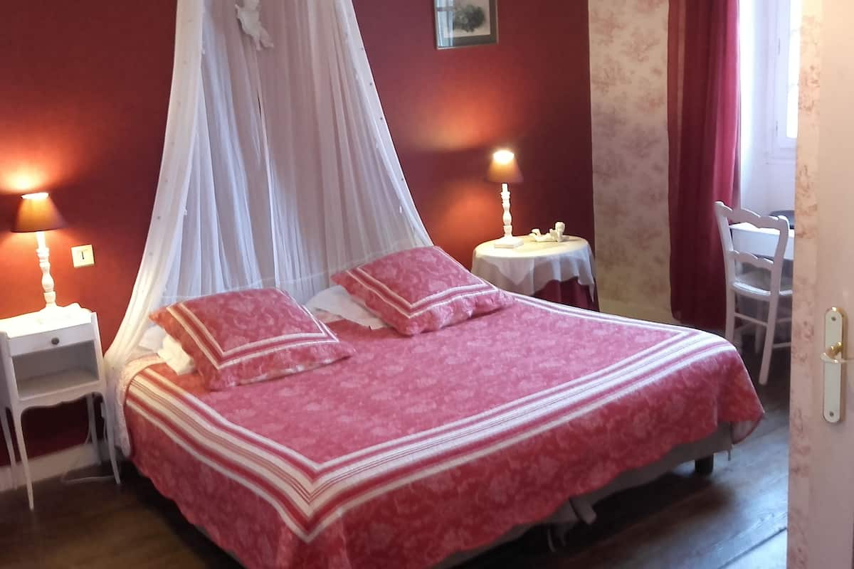 A bedroom with a four-poster bed, two bedside tables, and a small table with a lamp.