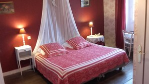 Un dormitorio con una cama con dosel, dos mesitas de noche y una pequeña mesa con lámpara.