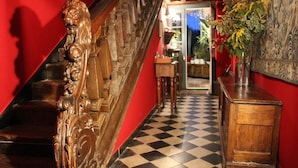 Una escalera con detalles de madera labrada, suelo a cuadros y pared roja.
